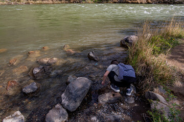 Young person with backpack crouching by the rocky riverbank of Charyn River