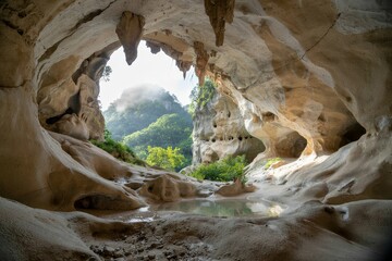 A photograph of a wide, cavernous opening in a limestone cliff face, revealing a stunning interior view
