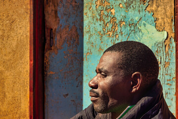 africa village, african man smiling , in front of the house in the yard, blue door, profile view