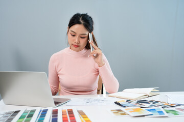 Concentrated young interior designer woman sitting at table with blueprint drawing ,swatches and...