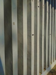 Concrete walls with strong white and grey vertical stripes, creating a repeating pattern of light and shadow, suggest architectural details or fencing.