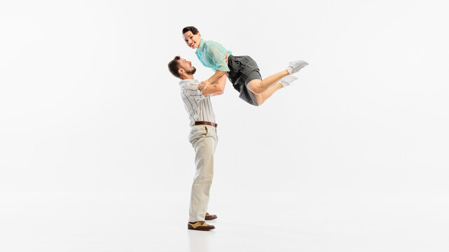 Two dancers in vibrant attire perform a retro dance lift against a white background. Concept of nostalgia and energetic dance moves revisiting past decades.