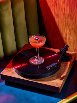 A red cocktail with raspberries stands on a vinyl turntable in a bar restaurant.