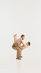 A retro couple performs a lively swing dance move in vintage-inspired attire against a white...