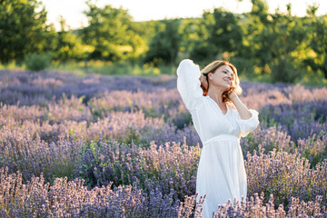 Beautiful woman enjoying summer breeze in lavender field. Portrait of blonde in sunlight....