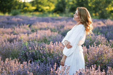 Beautiful woman enjoying summer breeze in lavender field. Portrait of blonde in sunlight....