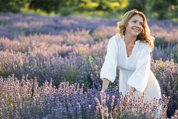 Beautiful woman enjoying summer breeze in lavender field. Portrait of blonde in sunlight....