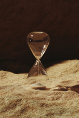 Minimalist hourglass on sand with dramatic light and shadows
