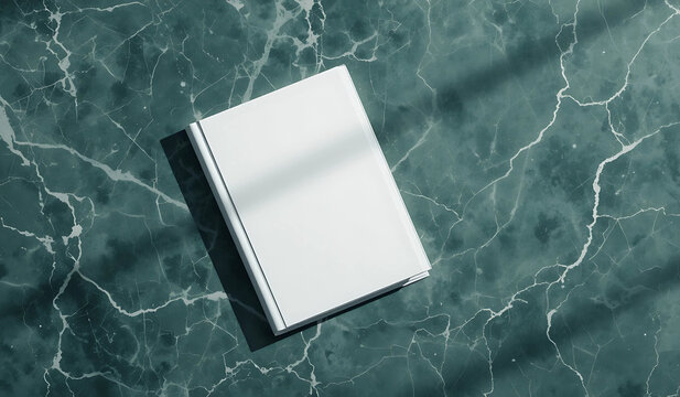 A blank white book cover rests on a dark teal marble surface, bathed in sunlight. Minimalist and elegant, perfect for book cover mockups or design presentations.