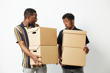 Two black men sharing a surprised moment while carrying cardboard boxes, showcasing their teamwork...