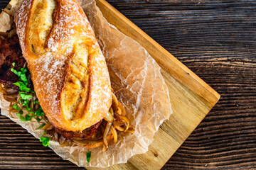 Takeaway sandwich with fried minced cutlets and caramelized onion on wooden table