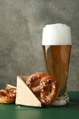 Tasty pretzels and glass of beer on green wooden table against grey textured background, closeup