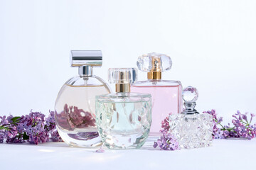 Perfume bottles and branches with lilac flowers on light grey background, closeup