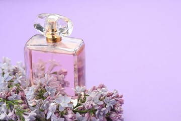 Bottle with perfume and lilac flowers on violet background, closeup. Space for text