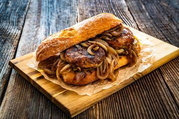 Takeaway sandwich with fried minced cutlets and caramelized onion on wooden table
