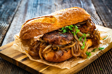 Takeaway sandwich with fried minced cutlets and caramelized onion on wooden table