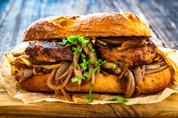 Takeaway sandwich with fried minced cutlets and caramelized onion on wooden table