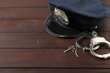 Police cap, handcuffs and keys on wooden table, closeup. Space for text