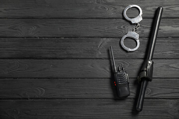 Police baton, walkie talkie and handcuffs on black wooden table, flat lay. Space for text