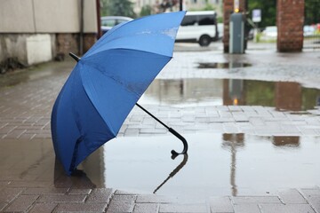 Blue umbrella on wet asphalt outdoors, space for text