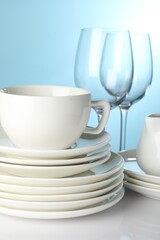 Different clean dishes on white table against light blue background, closeup