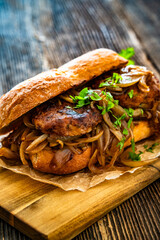 Takeaway sandwich with fried minced cutlets and caramelized onion on wooden table