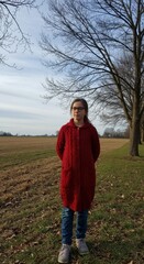 Girl in red sweater standing in serene countryside landscape with bare trees and open field