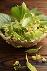 Beautiful linden flowers and leaves in wicker bowl on wooden table, closeup