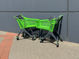 Two bright green shopping carts parked near a dark gray wall outside a store. Urban detail with contrast in colors