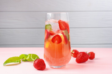Refreshing drink with strawberries, mint and ice on pink wooden table against grey background,...