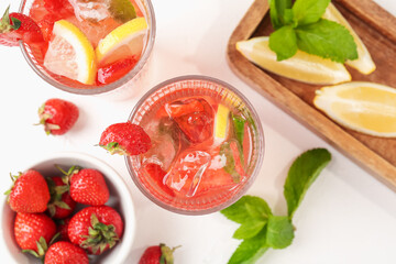 Refreshing drink with strawberries, mint, lemon and ice on white table, flat lay