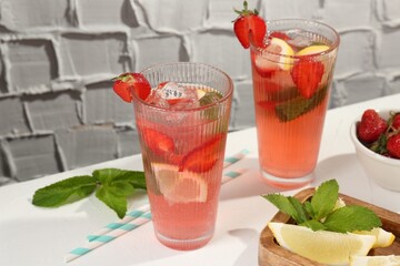 Refreshing drink with strawberries, mint, lemon and ice on white table against grey textured background, closeup