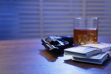 Mafia and criminal world. Gun, whiskey and money on wooden table indoors, closeup. Space for text