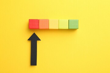 Maximum. Colorful cubes and arrow pointing at red one on yellow background, flat lay