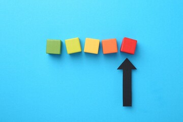 Maximum. Colorful cubes and arrow pointing at red one on light blue background, flat lay