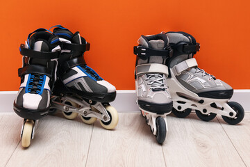 Pairs of roller skates on floor near orange wall