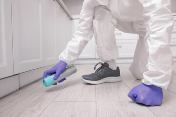 Pest control worker in protective suit spraying insecticide at home, closeup