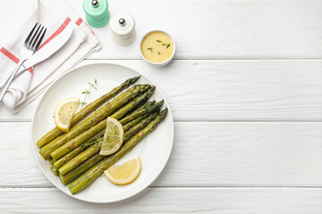 Tasty cooked asparagus served with lemon and thyme on white wooden table, flat lay. Space for text