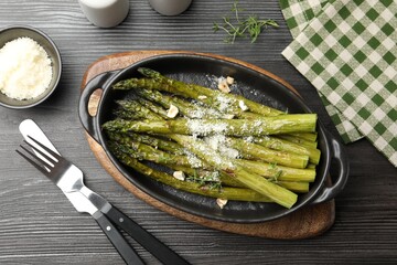 Tasty cooked asparagus served with parmesan on black wooden table, flat lay