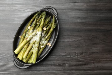 Tasty cooked asparagus served with parmesan on black wooden table, top view. Space for text