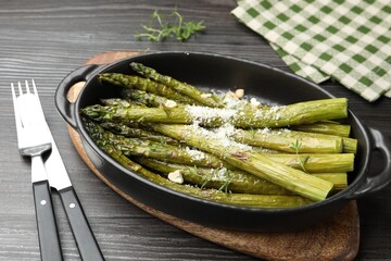 Tasty cooked asparagus served with parmesan on black wooden table, closeup