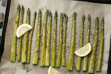 Tasty cooked asparagus and lemon on baking tray on wooden table, top view