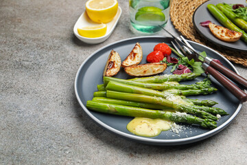 Tasty cooked asparagus served with baked potatoes, tomatoes and sauce on grey table, closeup. Space...