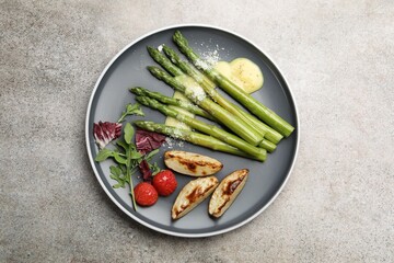 Tasty cooked asparagus served with baked potatoes, tomatoes and sauce on grey table, top view