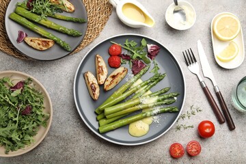 Tasty cooked asparagus served with baked potatoes, tomatoes and sauce on grey table, flat lay