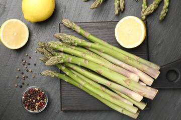 Fresh raw asparagus spears, lemon and spices on black table, flat lay