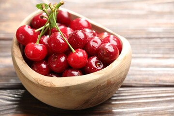 Fresh wet cherries in bowl on wooden table, closeup