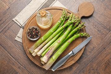 Fresh raw asparagus, spices, oil and knife on wooden table, top view