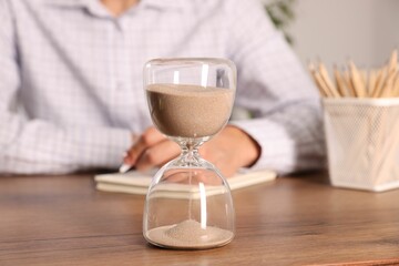 Deadline. Hourglass and man working at wooden table, selective focus