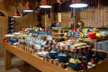 Original buffet table setup with Romanian cuisine featuring dried fish, vegetables, spreads, and wooden walls creating rustic dining atmosphere
